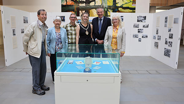 Six people standing around a display box with exhibition stands behind them, all displaying images and artefacts from the University of Worcester's 80 year history.