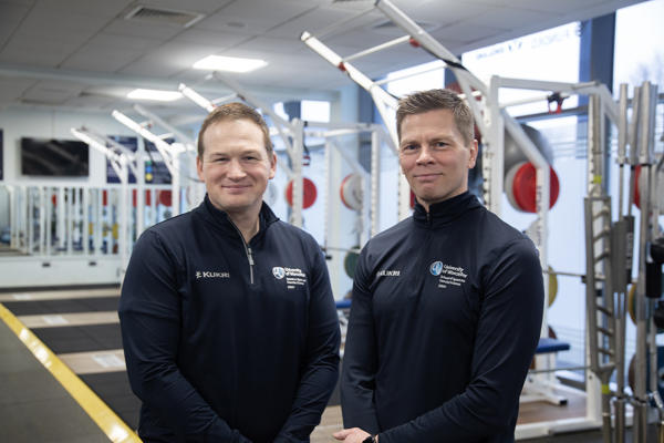 Two people posed looking at the camera with gym equipment in background