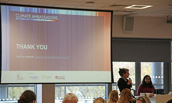 A projector screen displays a thank you message from the Climate Ambassadors and one person is standing next to the screen holiding a microphone while others are watching.