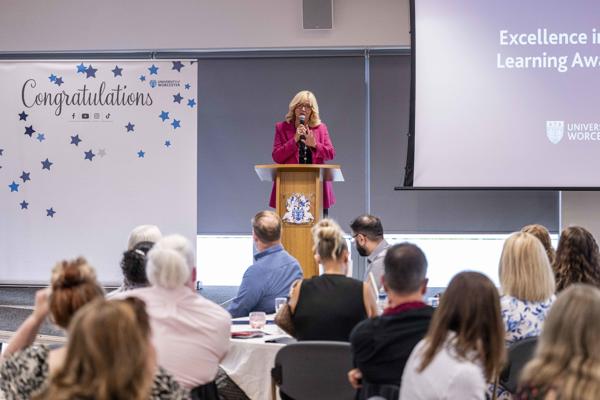 Professor Alison Machin standing at a podium delivering a speech in front of a room of people