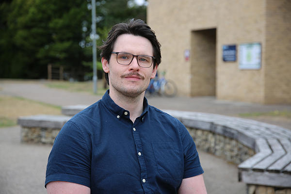 Person looking at camera with outside of a building and greenery behind them in background