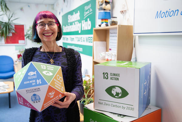 Person holding a cardboard shape with climate change messaging on it - standing in front of sign saying Student Sustainability hub