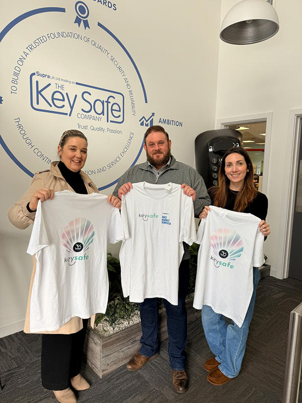 Three people standing in front of a Key Safe Company logo holding up t-shirts