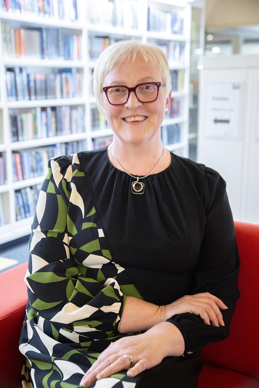 Photo of person sat on couch looking camera with rows of books behind