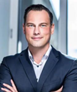 Lars-O Böckmann in suit attire smiling at camera with arms crossed