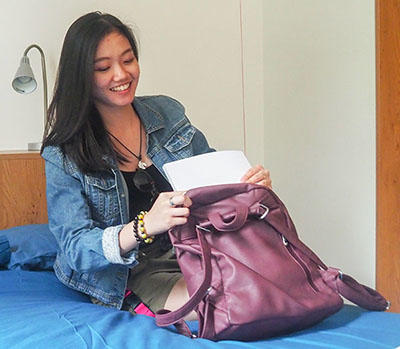 A smiling student is unpacking her bag in a bedroom
