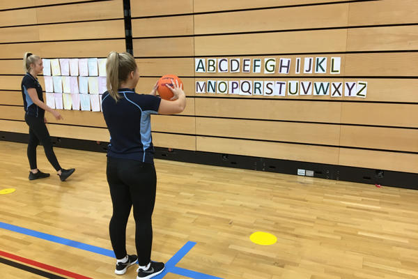 Two Adapted Sports students are throwing netballs against a wall with letter taped to it