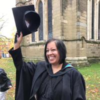 Woman in graduation robes holding a hat above her head