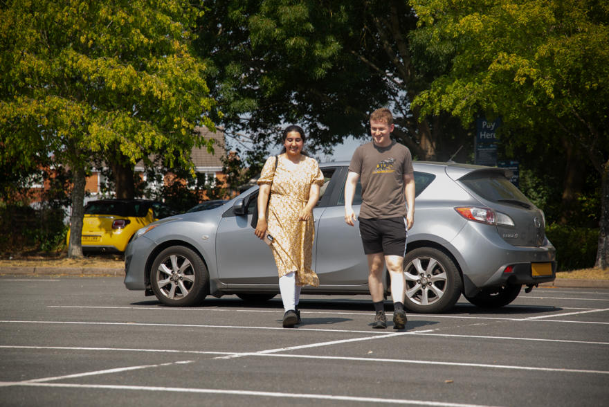 Two students walking away from their car in a large campus car park