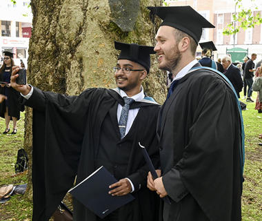 Two male students are taking photos of themselves during graduation