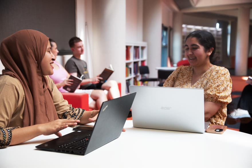 Students sat at tables with laptops out talking to each other in the library