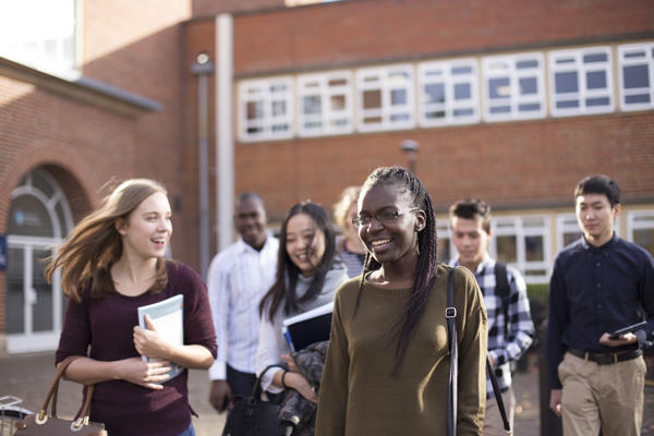 A group of students smiling holding leaflets walking by the main reception of St John's campus