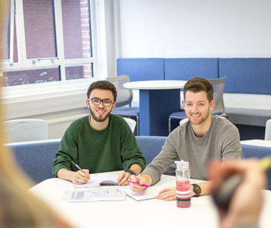 Two students are sitting facing a lecturer. They are both smiling.