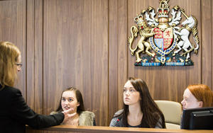Several students are sitting in the dock in the mock courtroom chatting to a lecturer