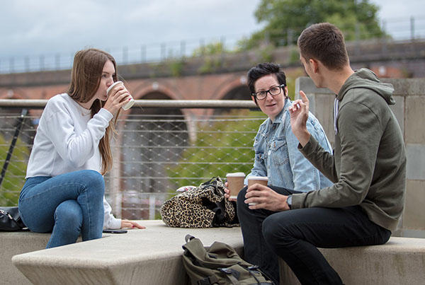 A group of students are sitting together outside the Hive drinking coffee