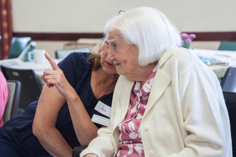 An elderly lady with white hair converses with a friend