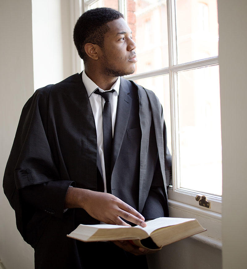 A student wearing Solicitor's robes is looking out of a window