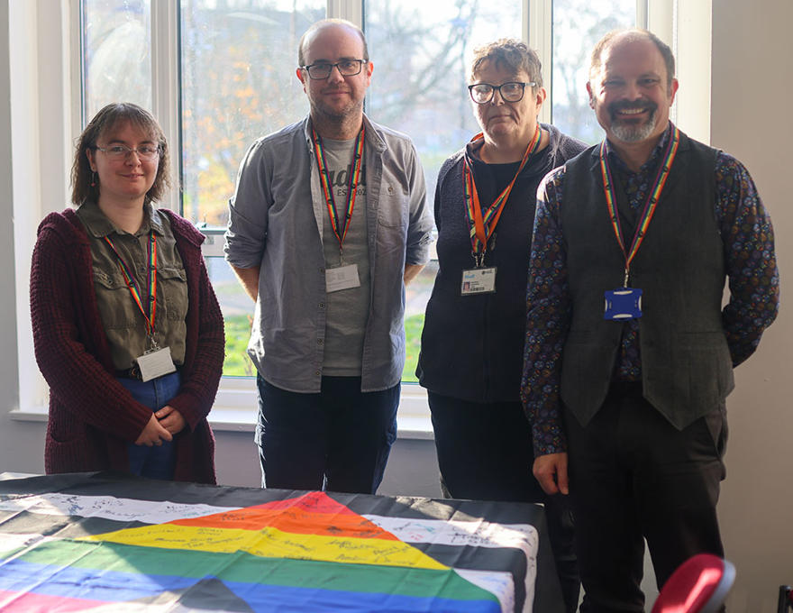 four members of staff wearing rainbow lanyards are smiling at the camera