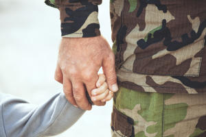 Close-up of a soldier in camouflage uniform holding a child's hand gently, symbolizing protection and care.