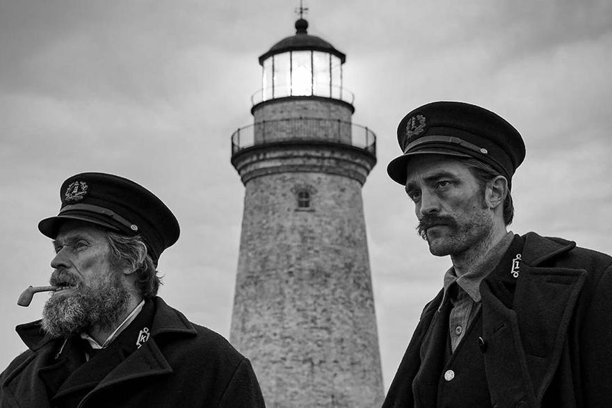 Two haggard men are standing net tow each other in front of a lighthouse