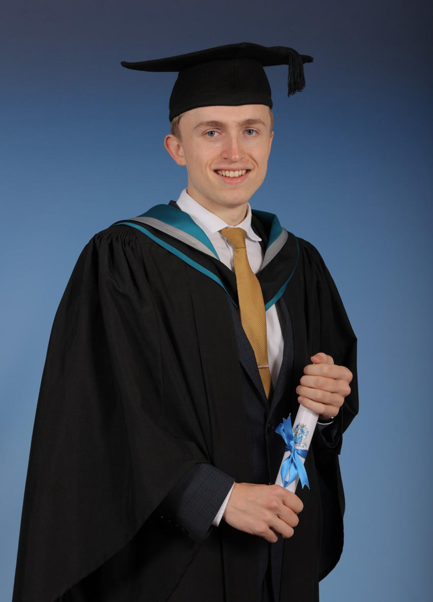 Graduate Wil in his graduation cap and gown holding his degree certificate