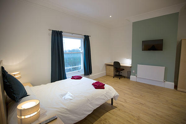 A large bedroom inside Barrington house. There is a large bed, a window, a desk and a television.