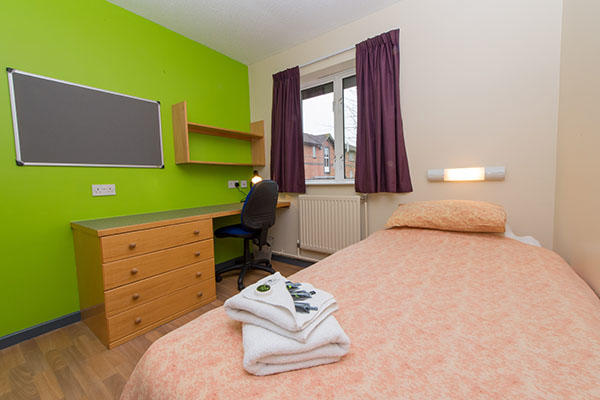 A bedroom inside University of Worcester accommodation. There is a single bed, a large pin board, desk, chest of drawers and a window in the room.