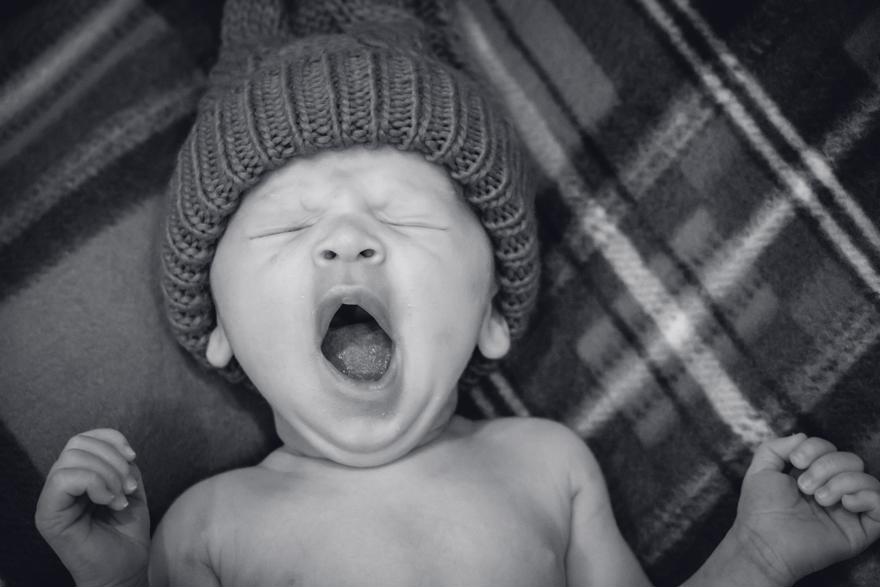 A baby wearing a woolly hat is yawning