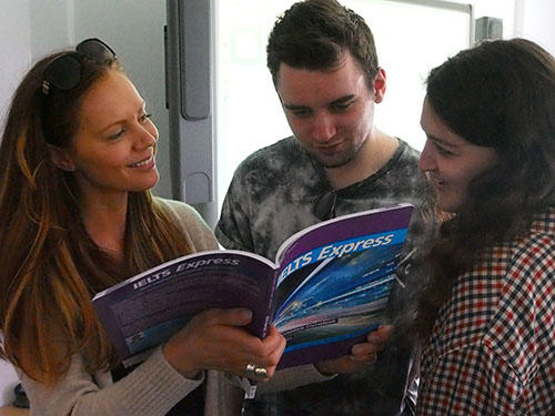Three students are looking over a CELTA course text book