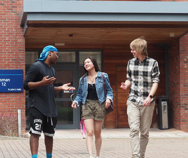 Three students are walking outside halls and enjoying the sunshine.