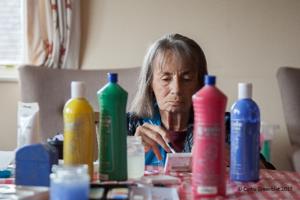 A lady paints using poster paints. The colourful bottles are placed in front of her.