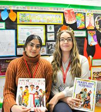 two students holding books in front of a colourful wall