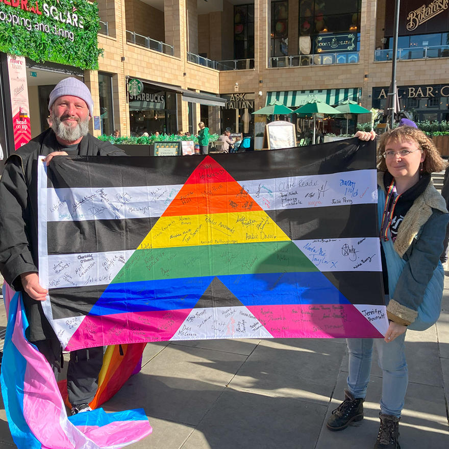 Staff holding the LGBTQ+ allies flag which is covered in staff signatures
