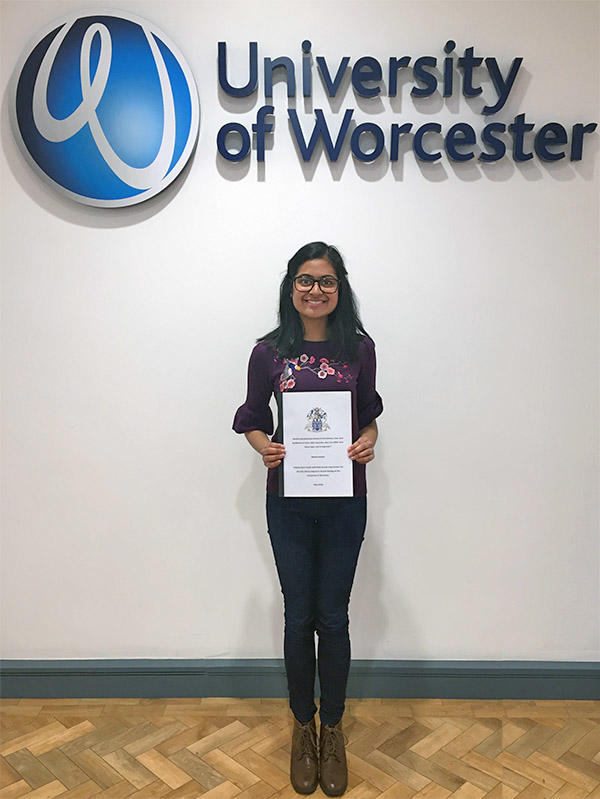 Meera Solanki is holding her graduation certificate. The University of Worcester logo is in the background.
