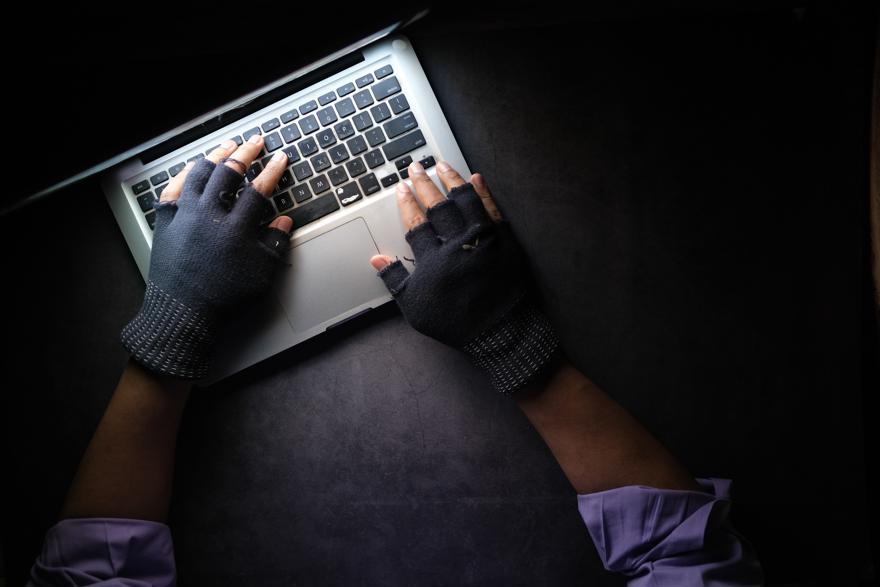 A man with black gloves on hacking a computer in a dark room