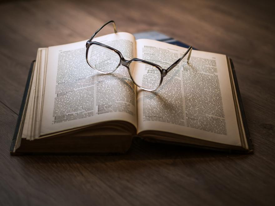 A pair of glasses sit atop of a large hardback book
