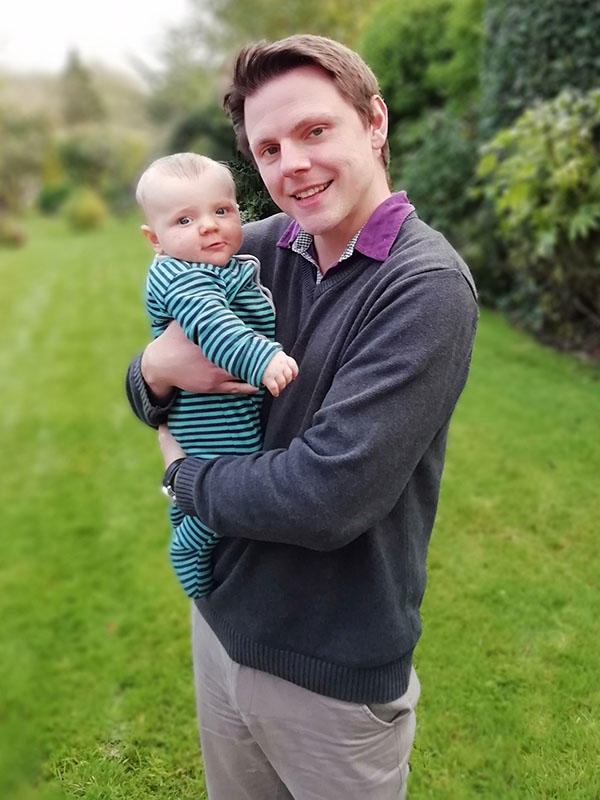 A smiling man holds his baby in a garden