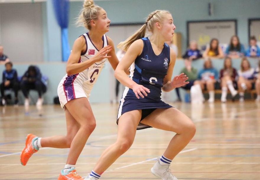 Two netball players in opposing team colours are competing for the ball