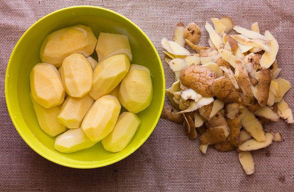 Some potatoes in a bowl next to some potato peelings