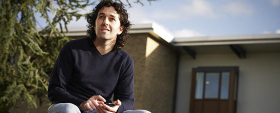 A student in a black top sits outdoors on his phone