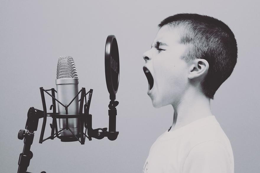 A child with short hair screams into a microphone