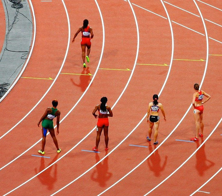 A group of runner dressed in brightly coloured lycra are standing on a running track