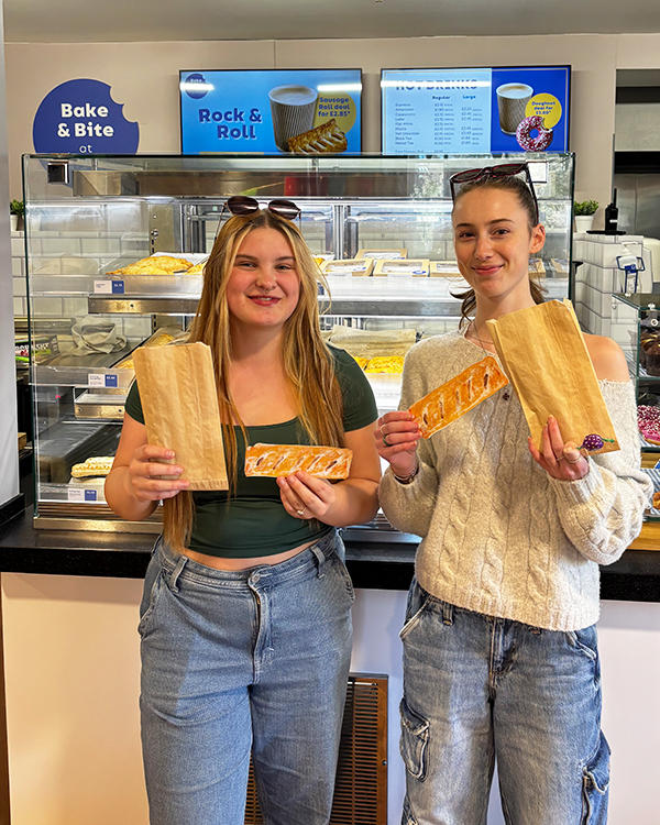 two students holding sausage rolls