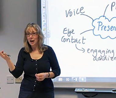 A woman is standing next to a whiteboard talking