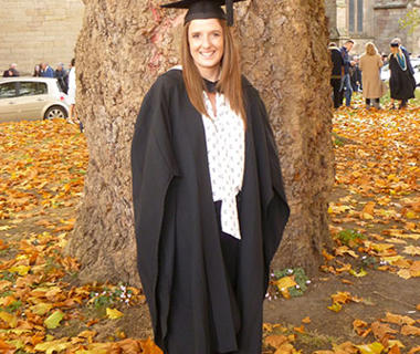 Student in graduation robes in front of a tree