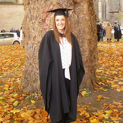 Student in graduation robes in front of a tree
