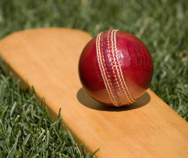 Close up shot of a wooden cricket bat and red ball laid on grass