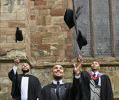 Three students dressed in graduation robes are throwing their mortar boards in the air