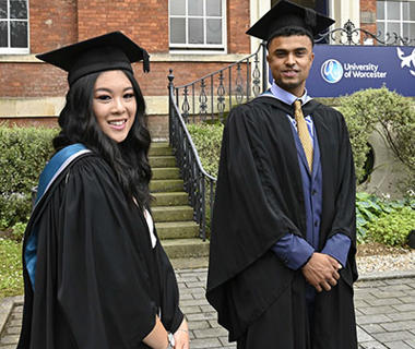 Two students in Graduation robes are smiling and looking at the camera