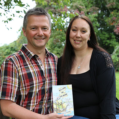 Man in checked shirt and woman in black top holding a book